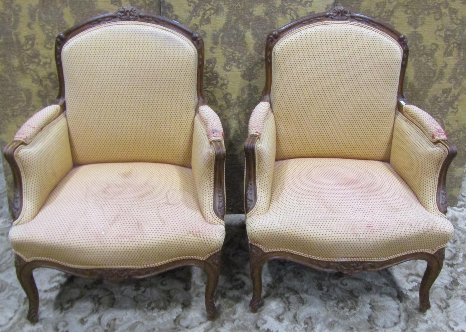 A pair of upholstered armchairs with carved show wood frames on cabriole supports