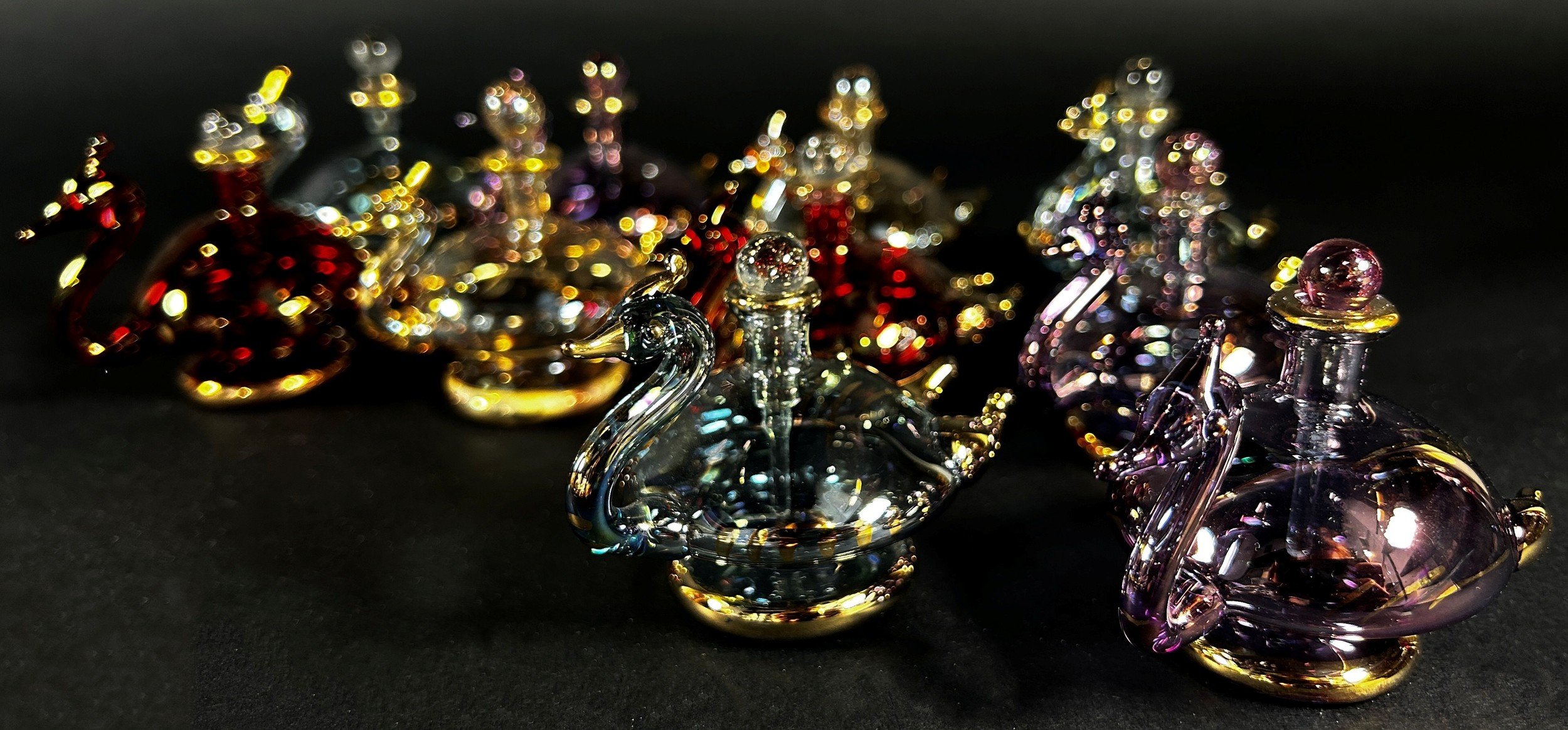 Ten iridescent gilded blown glass swan perfume bottles, together with a pink flamingo perfume