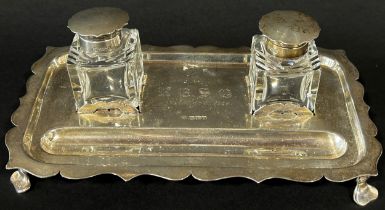 A silver pen and ink desk stand with two glass ink wells with silver caps, raised on splayed feet,