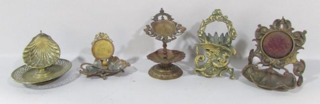 Five 19th century brass watch stands, mostly in the classical style of scrolls, laurels and shells.