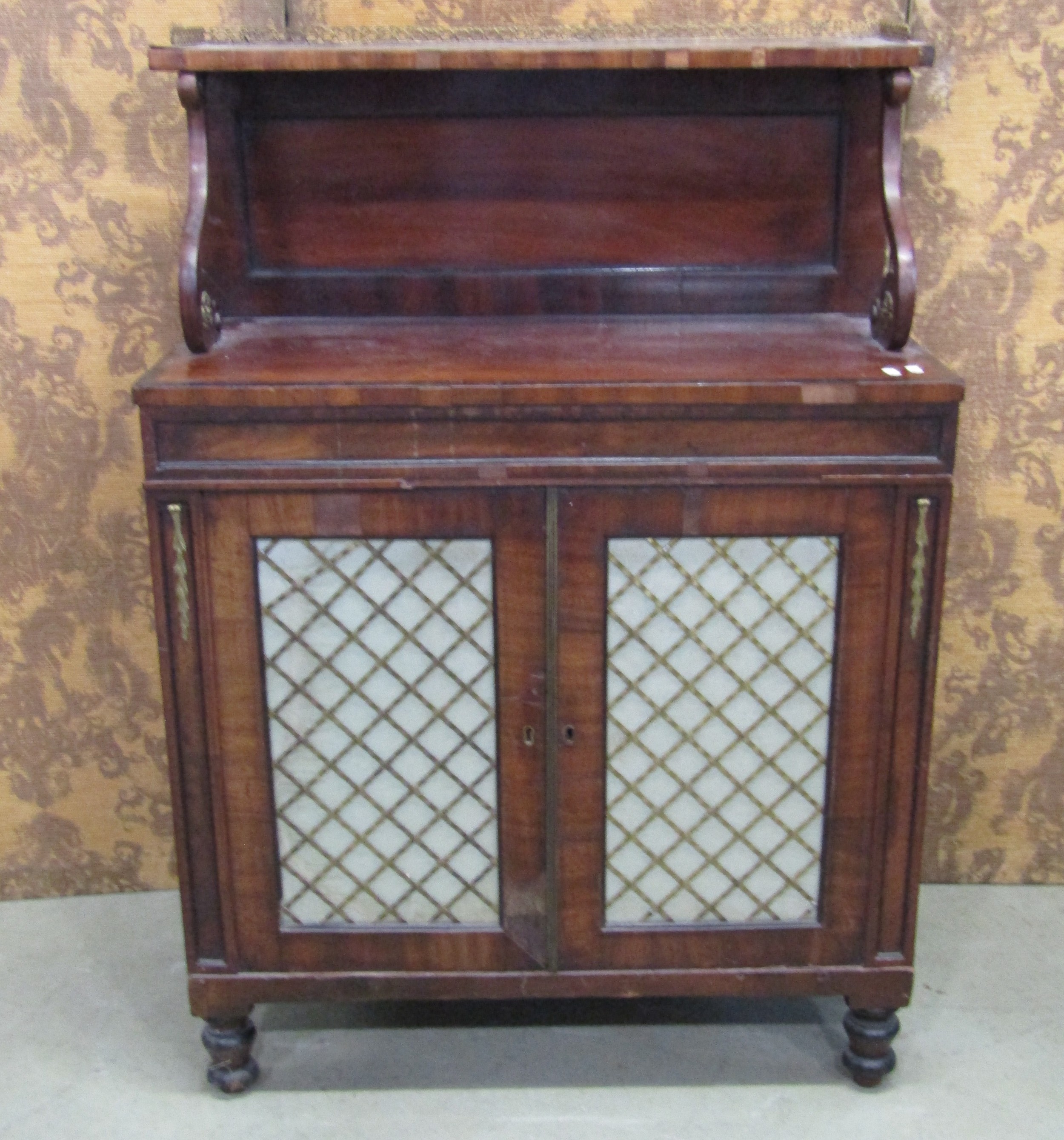 A Regency mahogany Chiffonier enclosed by two brass grilled doors beneath a raised and shaped back