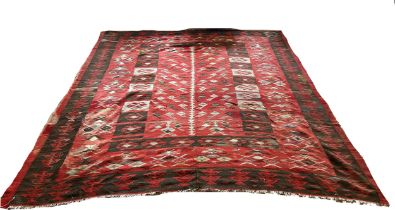 A Balkan Kilim with a repeating geometric pattern on a red ground, worn and with tears, 285 x