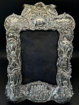 A Victorian silver photograph frame with military engravings of soldiers, weapons, battle fields,