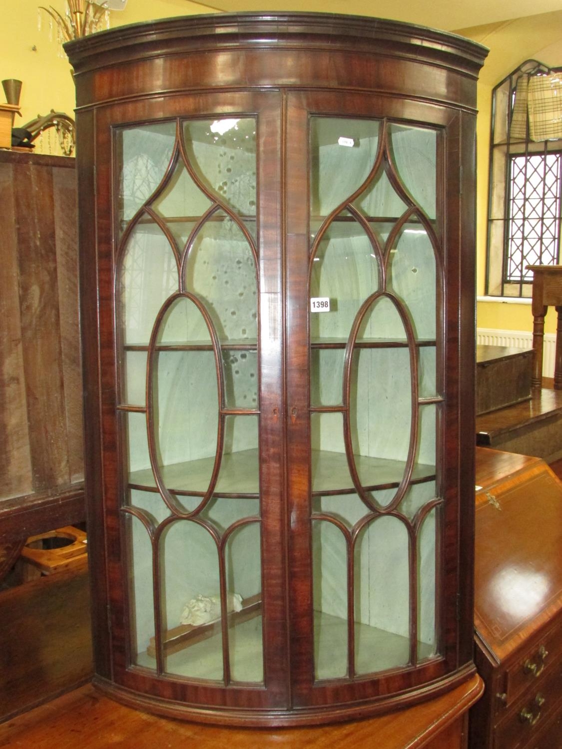 A Regency mahogany bow fronted hanging corner cupboard with astragal glazed panelled doors, original