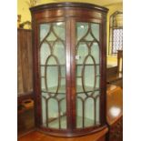 A Regency mahogany bow fronted hanging corner cupboard with astragal glazed panelled doors, original