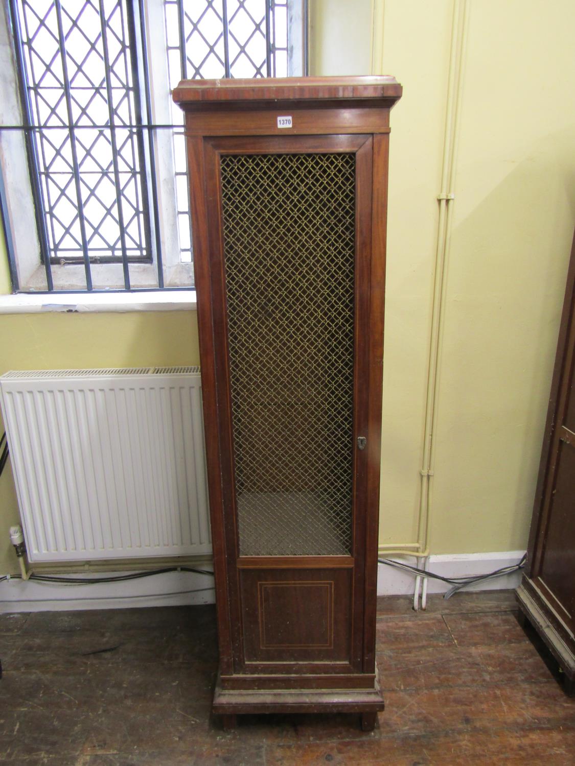 19th century cupboard of square cut tapering form enclosed by a brass grilled door, 50cm wide