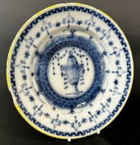 An 18th century tin glazed plate in a blue and white colourway, the central urn within further