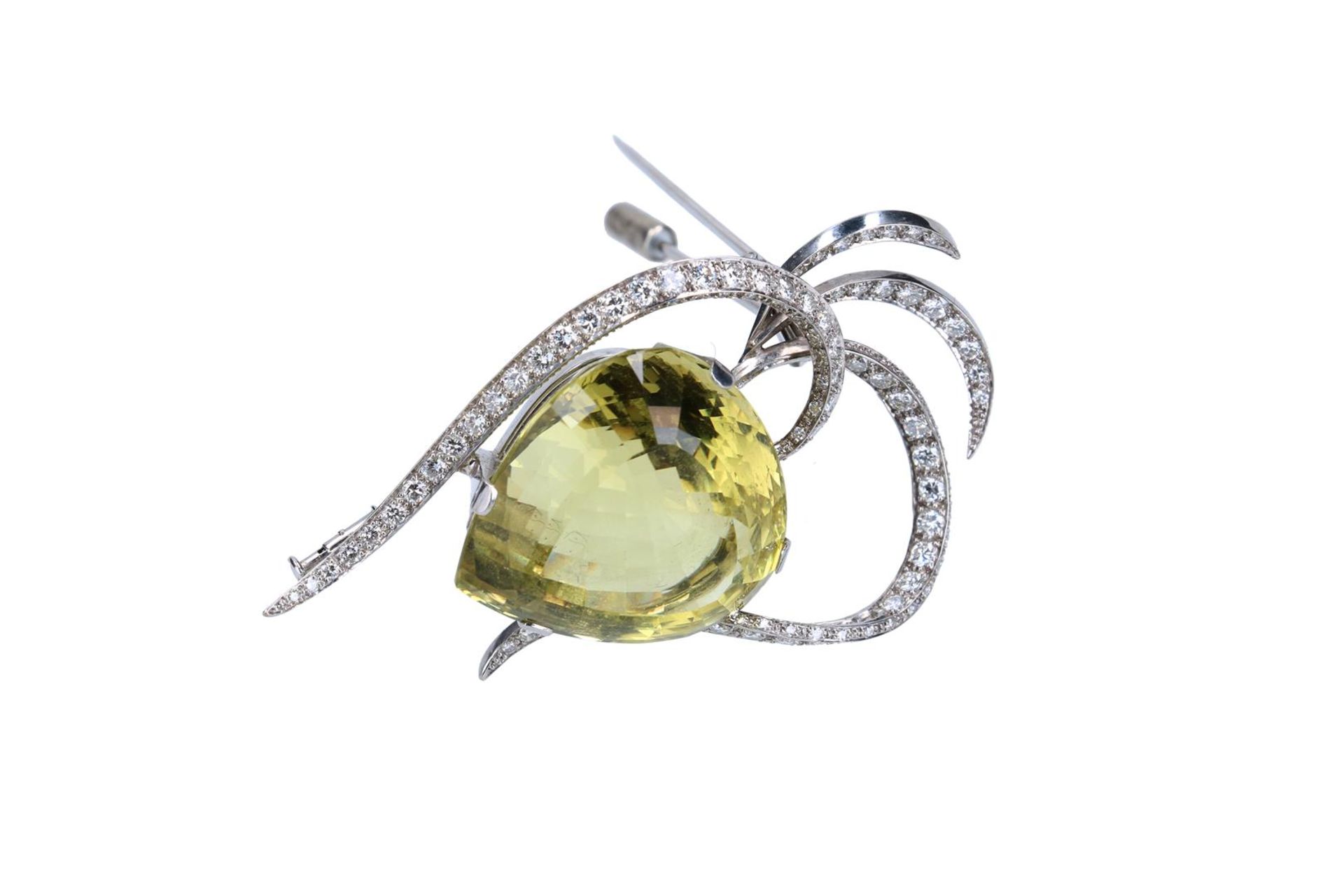 An 18-kt white gold brooch, set with a lemon citrin, of approx. 62 ct., surrounded by single and bri