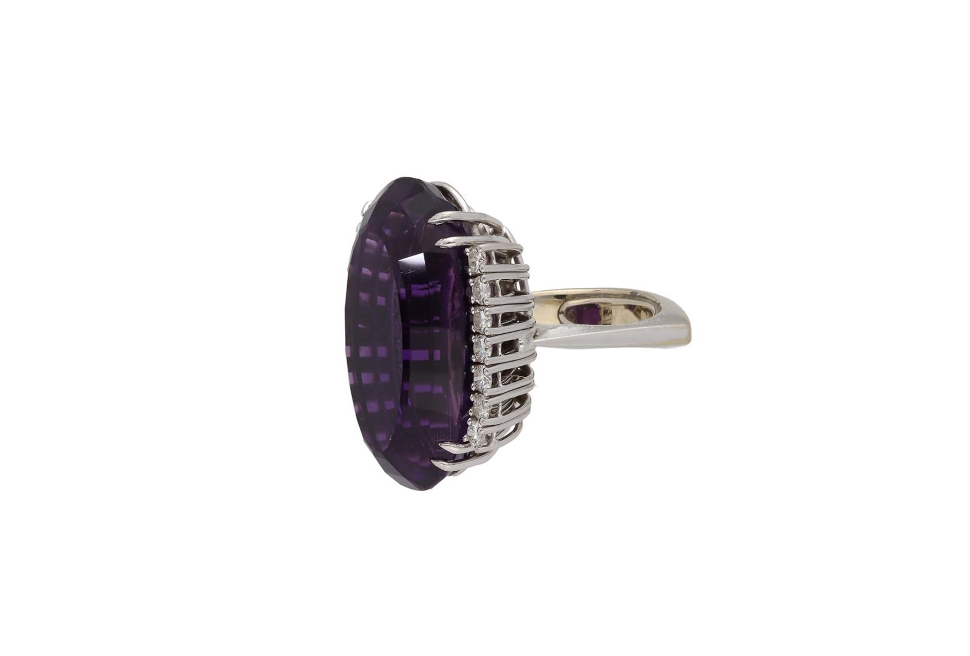 A 18-kt white gold ring, set with an oval cut amethyst of approx. 28,97 ct. flanked by brilliant cut - Image 2 of 4