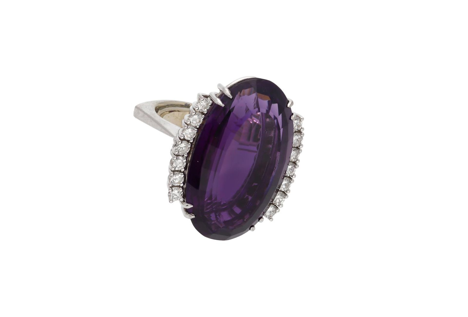 A 18-kt white gold ring, set with an oval cut amethyst of approx. 28,97 ct. flanked by brilliant cut