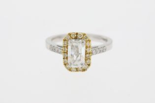 Stamped 18K and partial hallmark. An emerald cut diamond ring with a halo of yellow diamonds.