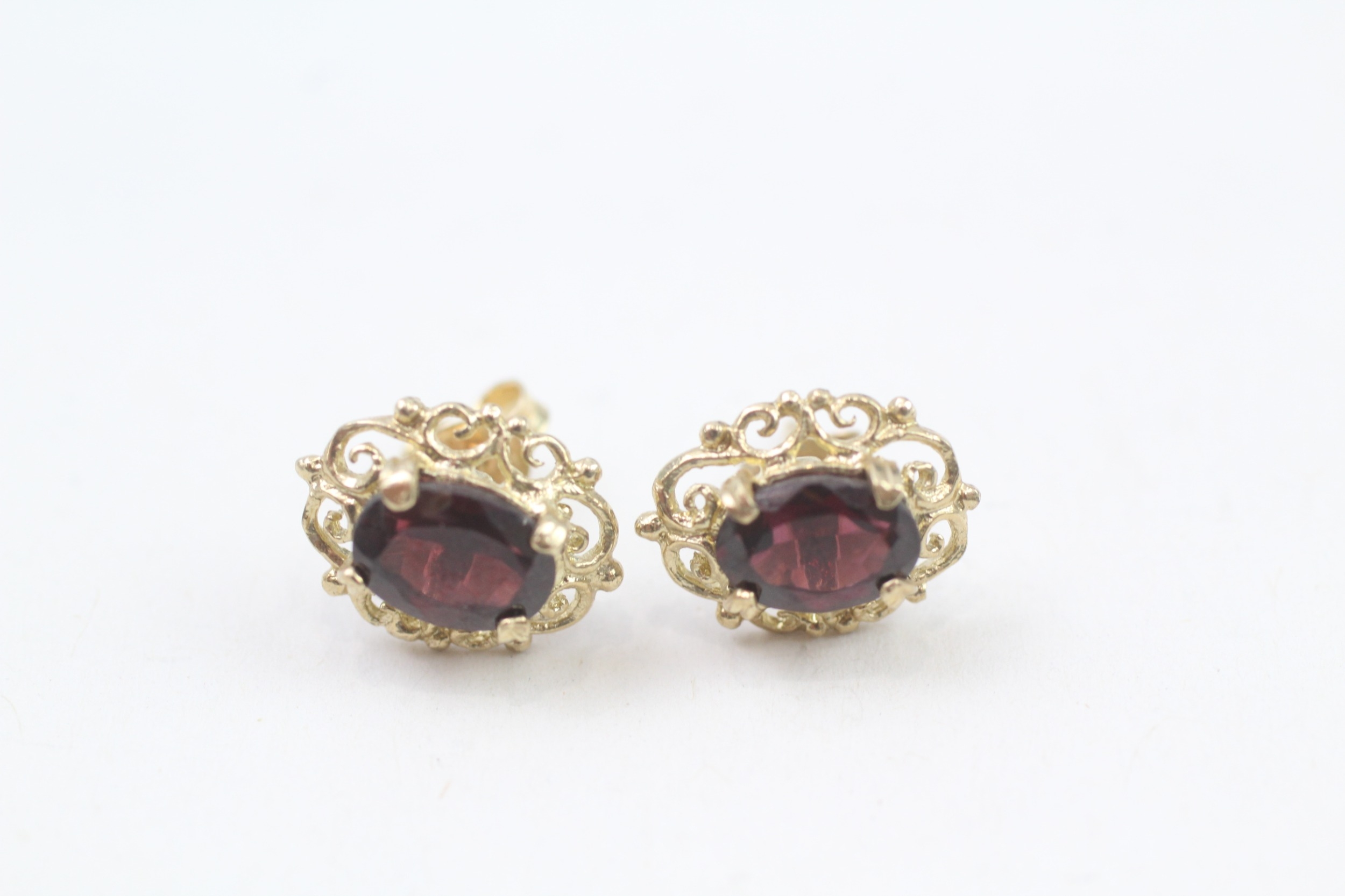 9ct gold oval cut garnet stud earrings with a scroll patterned border (1.7g)