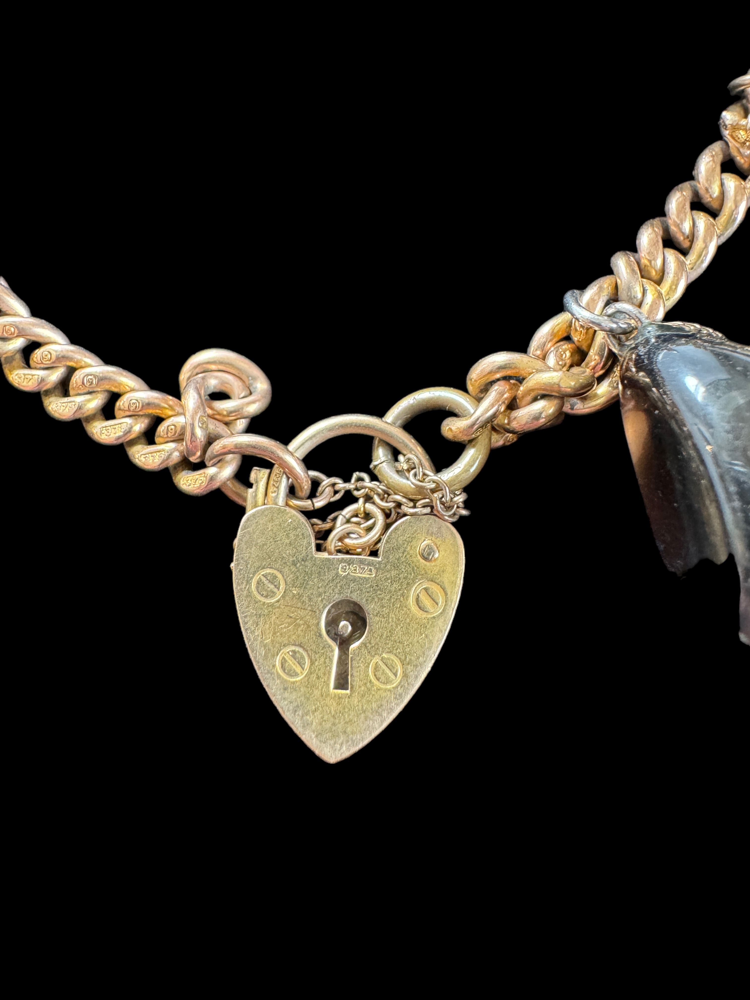 A 9ct gold curblink bracelet with 9ct gold heart padlock clasp and hung with ten charms, 1960s - Image 5 of 5