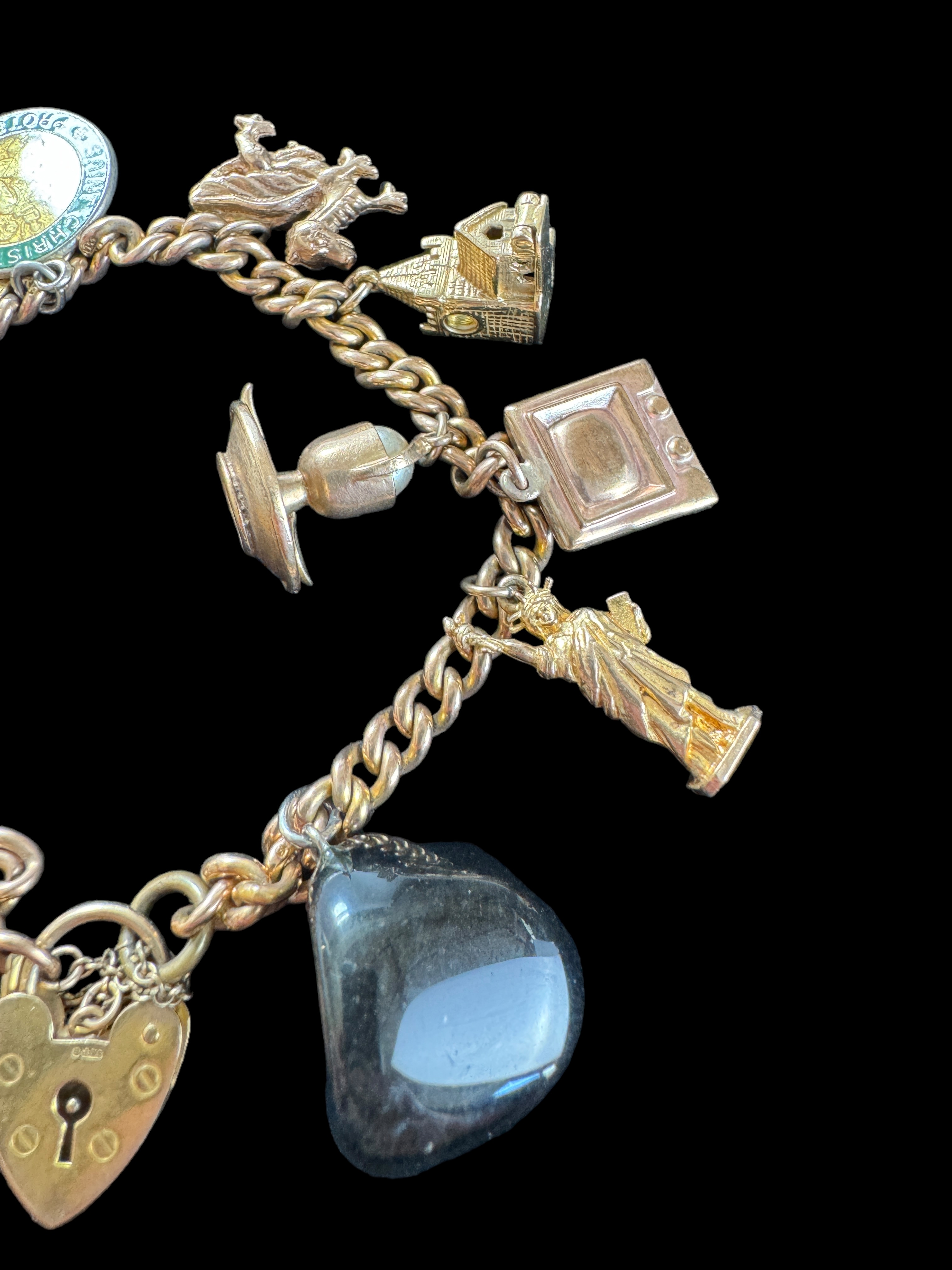 A 9ct gold curblink bracelet with 9ct gold heart padlock clasp and hung with ten charms, 1960s - Image 2 of 5
