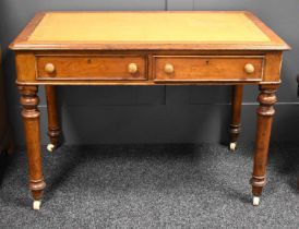 A Victorian oak two drawer writing desk with mustard coloured leather top, turned legs raised on