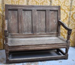 An 18th century oak or elm settle, the high back having a four panel backrest and shaped open