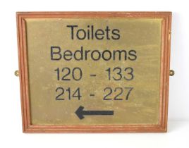A vintage brass hotel sign showing the directions for Toilets and Bedrooms.