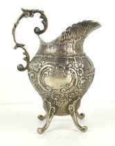 A continental silver cream jug with repousse floral decoration centred by a vacant rococo scroll