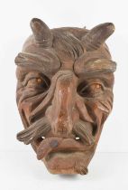 A 20th century wooden carved horned devil face mask, set with bead eyes, 38cm high.
