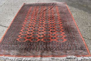 A red ground wool rug, with geometric central panel and stylised borders, 306cm by 230cm.