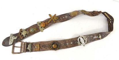 A vintage leather belt adorned with various regimental cap badges, including the Royal Sussex, The