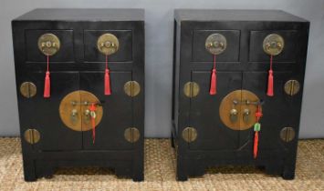 A pair of Chinese black lacquered cabinets, two short over two cupboard doors, with circular brass