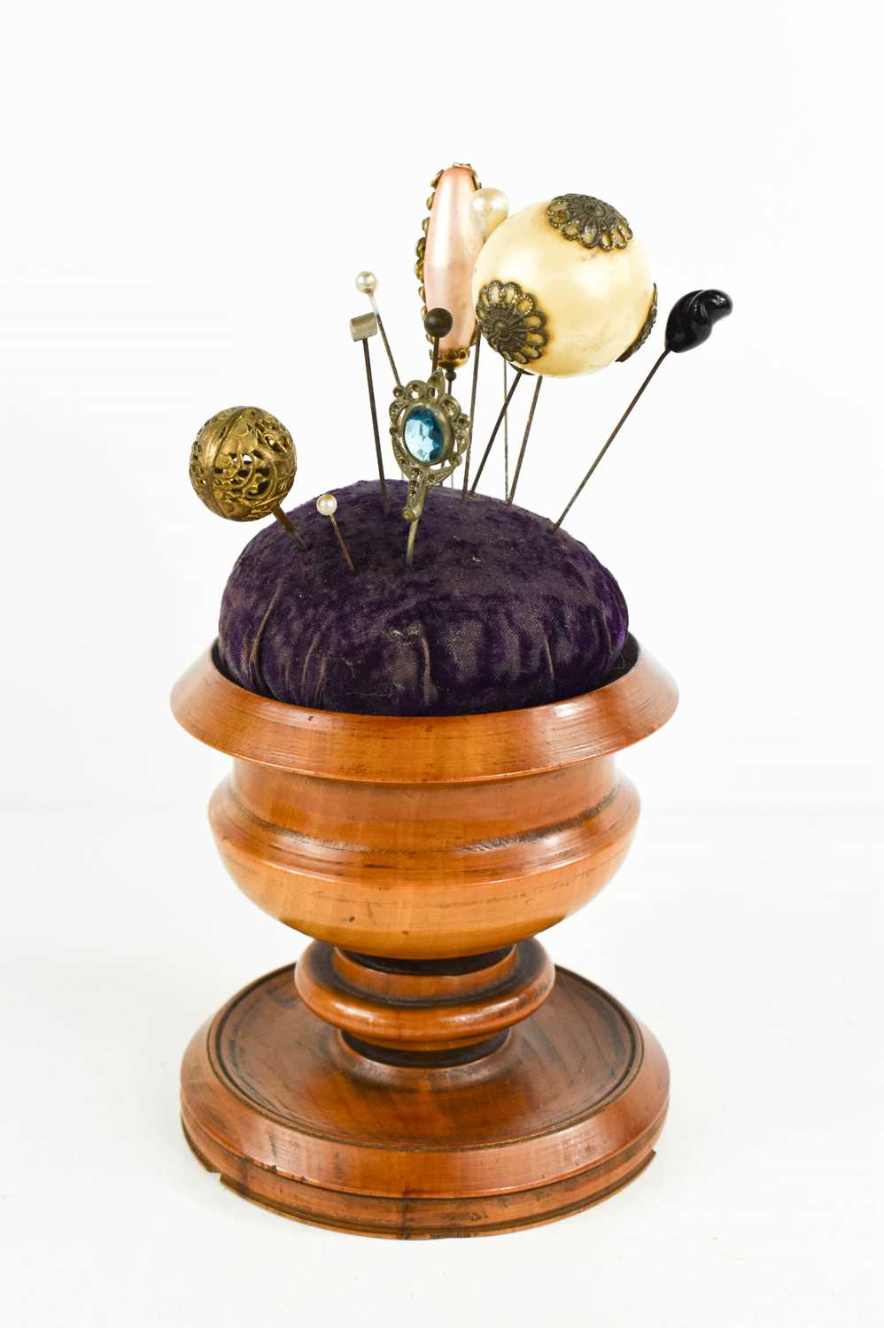 A 19th century treen pin cushion stand, with various hat pins, the turned pedestal stand housing the