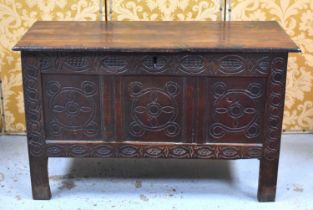 A 17th century oak coffer with planked lid and later carved three panel front raised on stile