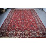 A large Middle Eastern wool rug with red ground, the centre decorated with stylised flowers with