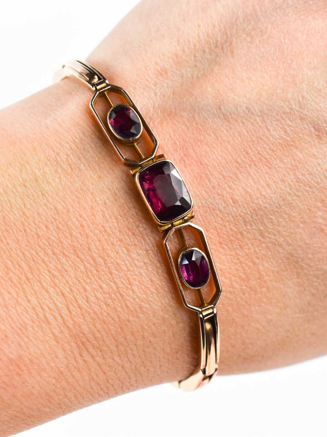 A 9ct rose gold bracelet set with three amethysts, the central emerald cut amethyst of approximately