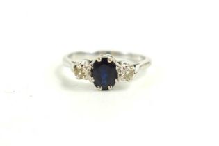 An 18ct white gold, sapphire and diamond three stone ring, the central oval dark sapphire of