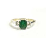 An 18ct white gold emerald and diamond, three stone ring, the emerald cut central stone of