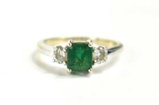 An 18ct white gold emerald and diamond, three stone ring, the emerald cut central stone of