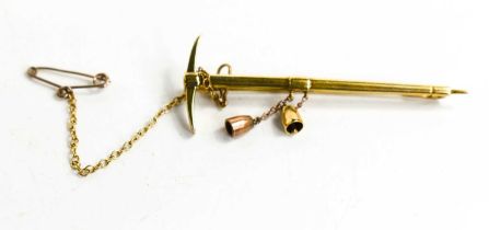 A gold tie pin in the form of a pick axe, with two pendant bells, a safety chain and presentation