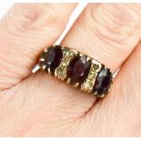 A 9ct gold and garnet three stone ring, each oval cut garnet interspersed with triplet of diamond