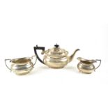 A silver three piece tea set, the teapot having an ebonised handle and decorated with gadrooned rim,