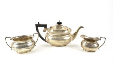 A silver three piece tea set, the teapot having an ebonised handle and decorated with gadrooned rim,