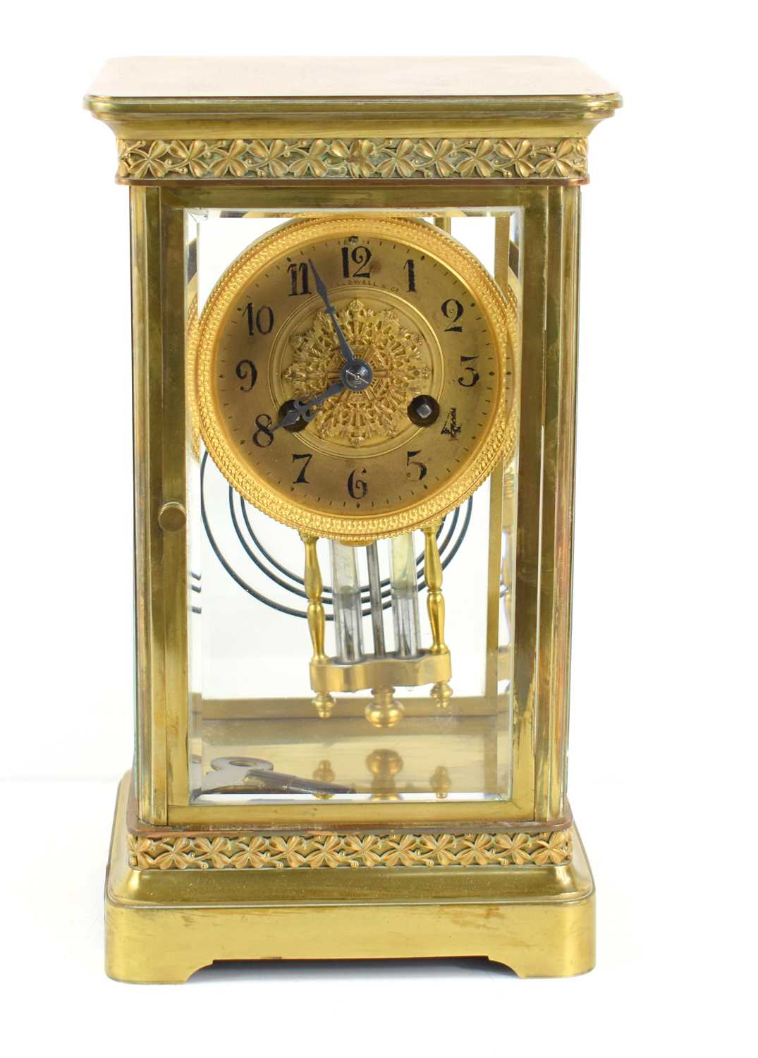 An antique J.E Caldwell & Co mantle clock, the clock suspended in a gilded brass and glass case,