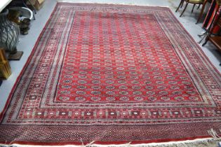A large wool rug, red ground, with geometric stylised borders and central panel, 285cm by 360cm.