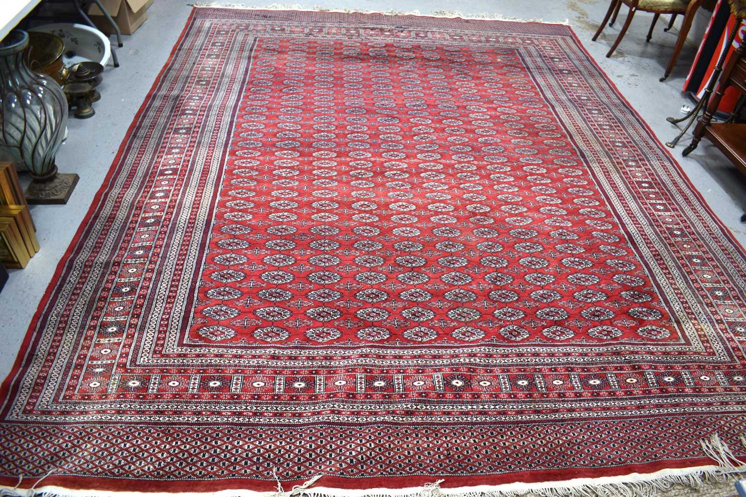 A large wool rug, red ground, with geometric stylised borders and central panel, 285cm by 360cm.