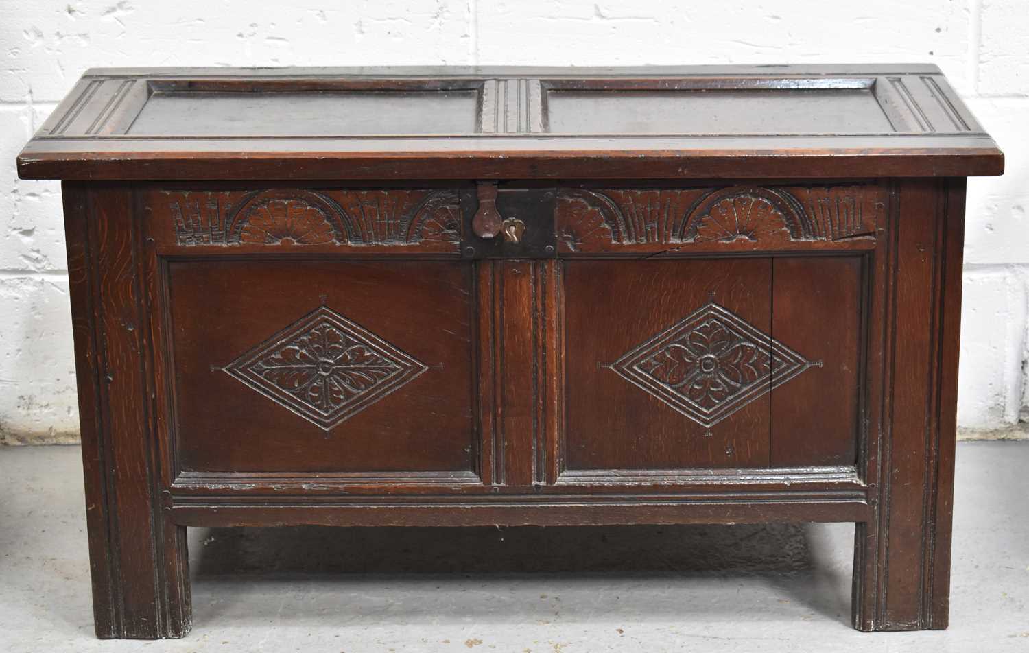 A 17th century oak coffer with two panel lid and front, the lunette carved top rail housing lock