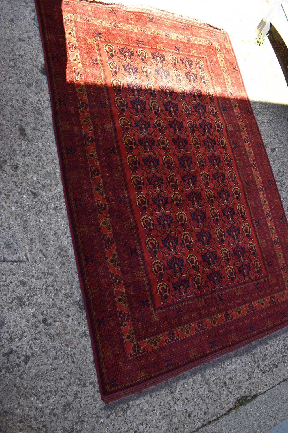 A Middle eastern red ground rug decorated with stylised floral motifs and stylised borders and