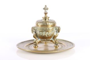 Indian brass inkwell raised on ram mask and dolphin supports, 19cm diameter.