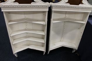 Pair of cream painted wall mounted bookcases with scroll pediments, 106cm tall.