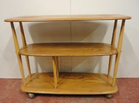 Ercol blonde elm console bookcase with three tiers, on turned uprights and castors, label to the