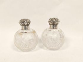 Pair of cut glass globular scent bottles with embossed silver caps.