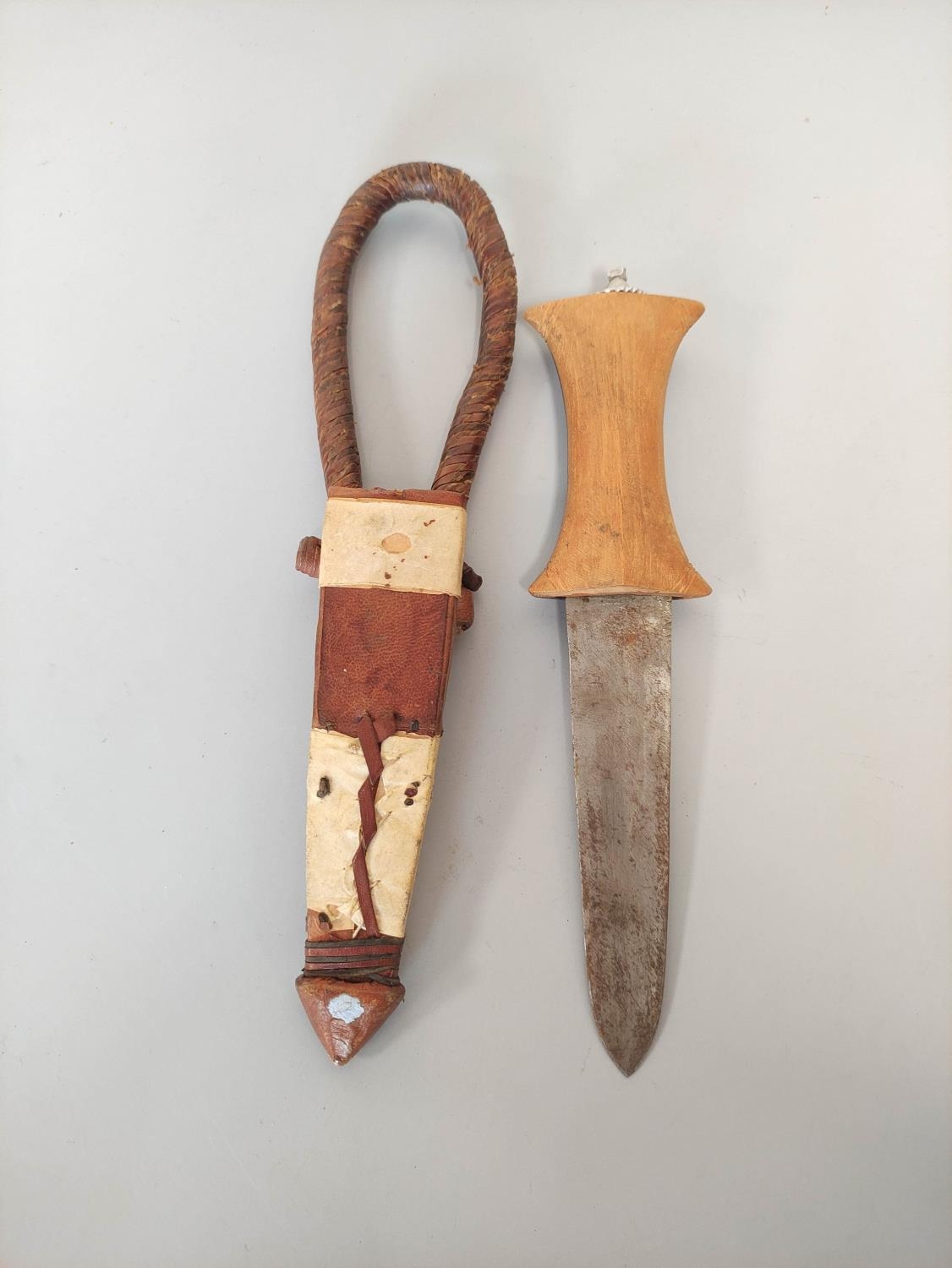 A Sudanese arm knife with tapering straight blade and carved wooden hilt. Contained in tooled