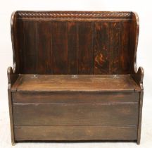 In the manner of Titchmarsh and Goodwin, an oak settle with panelled back and hinged seat, revealing