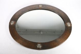 In the manner of Liberty and Co., an Arts & Crafts oval mirror, c1900, the hammered copper frame