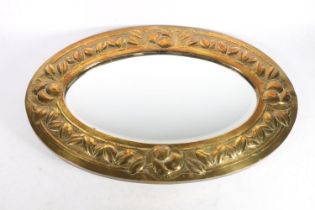 Arts and Crafts oval mirror, c1905, the hammered brass frame embossed with fruit and leaves